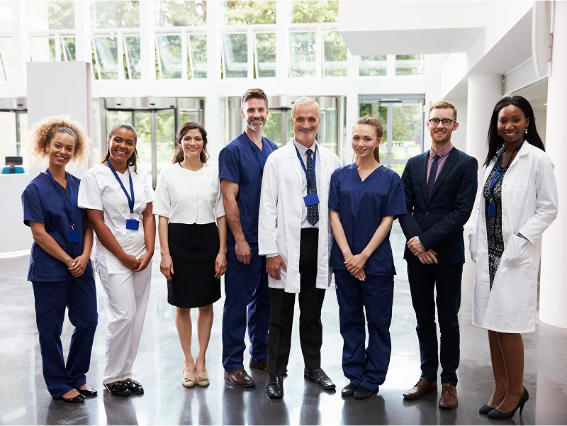 A group of eight healthcare professionals, including doctors and nurses, standing in a well-lit hospital lobby, smiling at the camera.